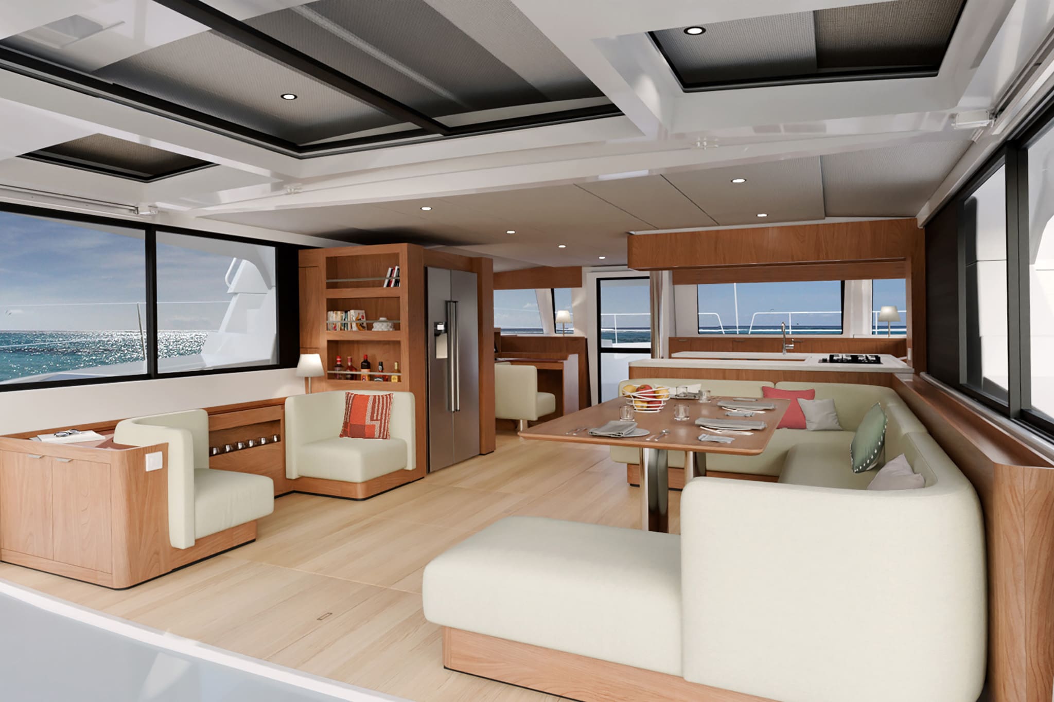 Catamaran saloon interior with cream upholstered seating, wooden cabinetry, dining table, and panoramic windows overlooking open water — the saloon is the main communal cabin where crew eat, navigate, and gather