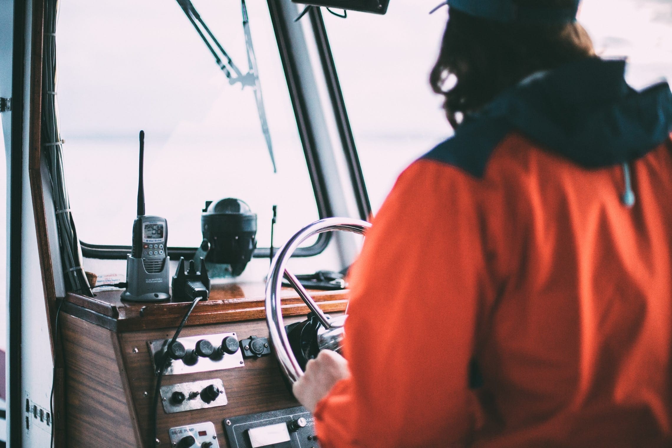 Helmsman at the wheel of a sailing yacht with chart plotter and compass visible on the binnacle — the helm is the wheel or tiller used to steer the boat by controlling the rudder